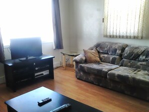 A living room with a flat-screen TV on a stand, a couch with a patterned cover, and a coffee table with a remote control.