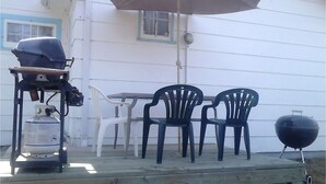 A patio with a table and chairs, a grill, a propane tank, and an umbrella. - Canora Home Rentals Holiday Cottage (Canora)