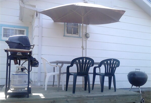A patio with a table and chairs, a grill, a propane tank, and an umbrella.