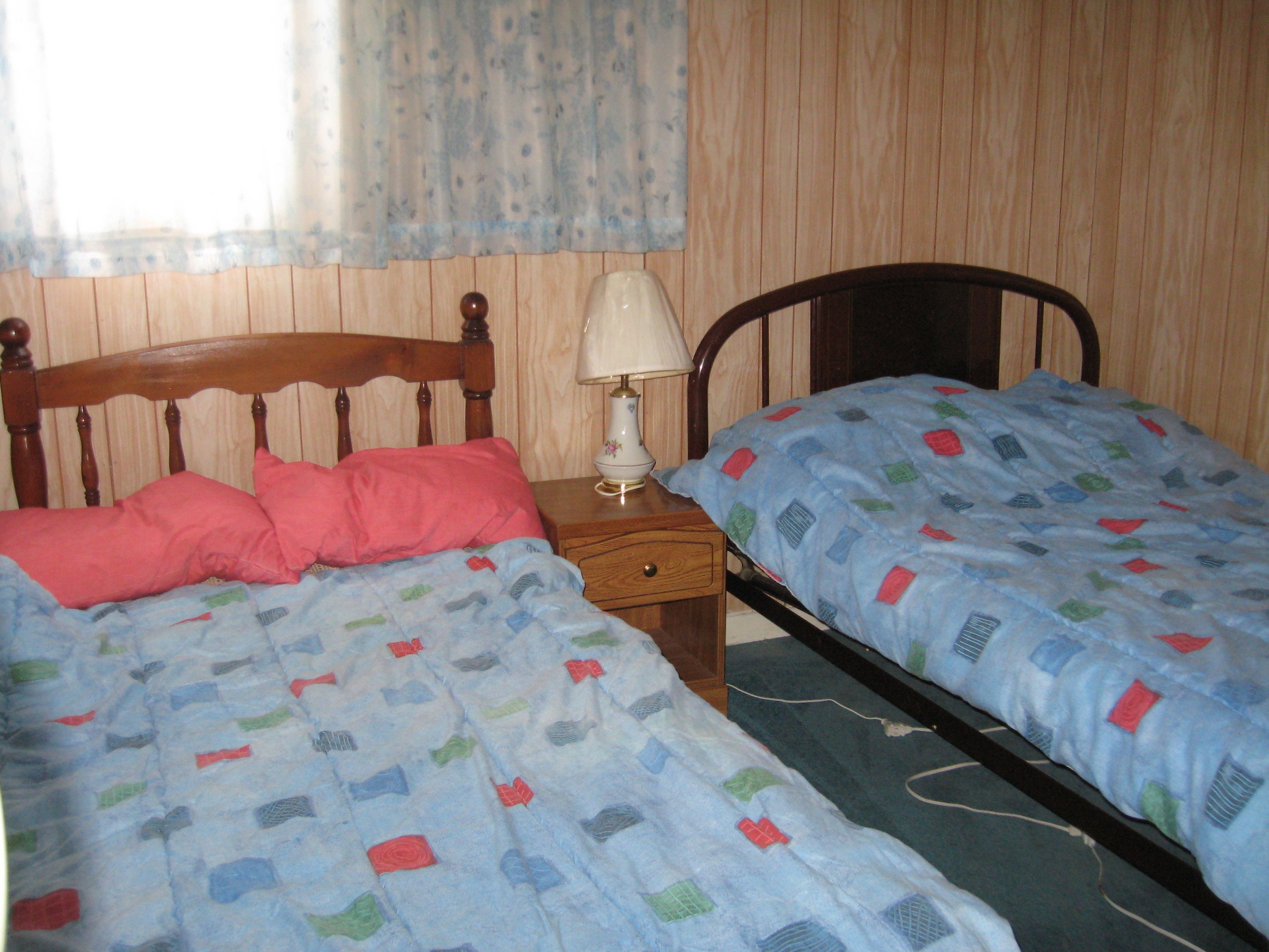 Een slaapkamer met twee bedden, houten hoofdborden, een nachtkastje met een lamp en een raam met gordijnen.