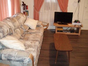 A living room with a sofa, a television on a wooden stand, and a small table with electronic devices.