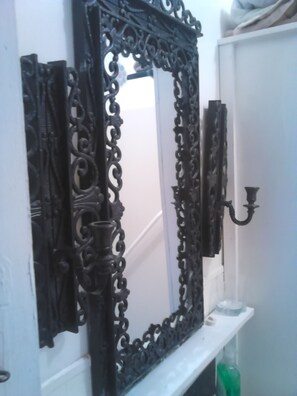 A bathroom with a large ornate mirror, a white sink, and a green bottle on the counter.
