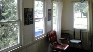 A room with a wooden ceiling and large windows. There are two chairs and a small table. - Canora Home Rentals Holiday Cottage (Canora)