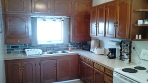 A kitchen with wooden cabinets, a double sink, a toaster, and a stove. - Canora Home Rentals Holiday Cottage (Canora)