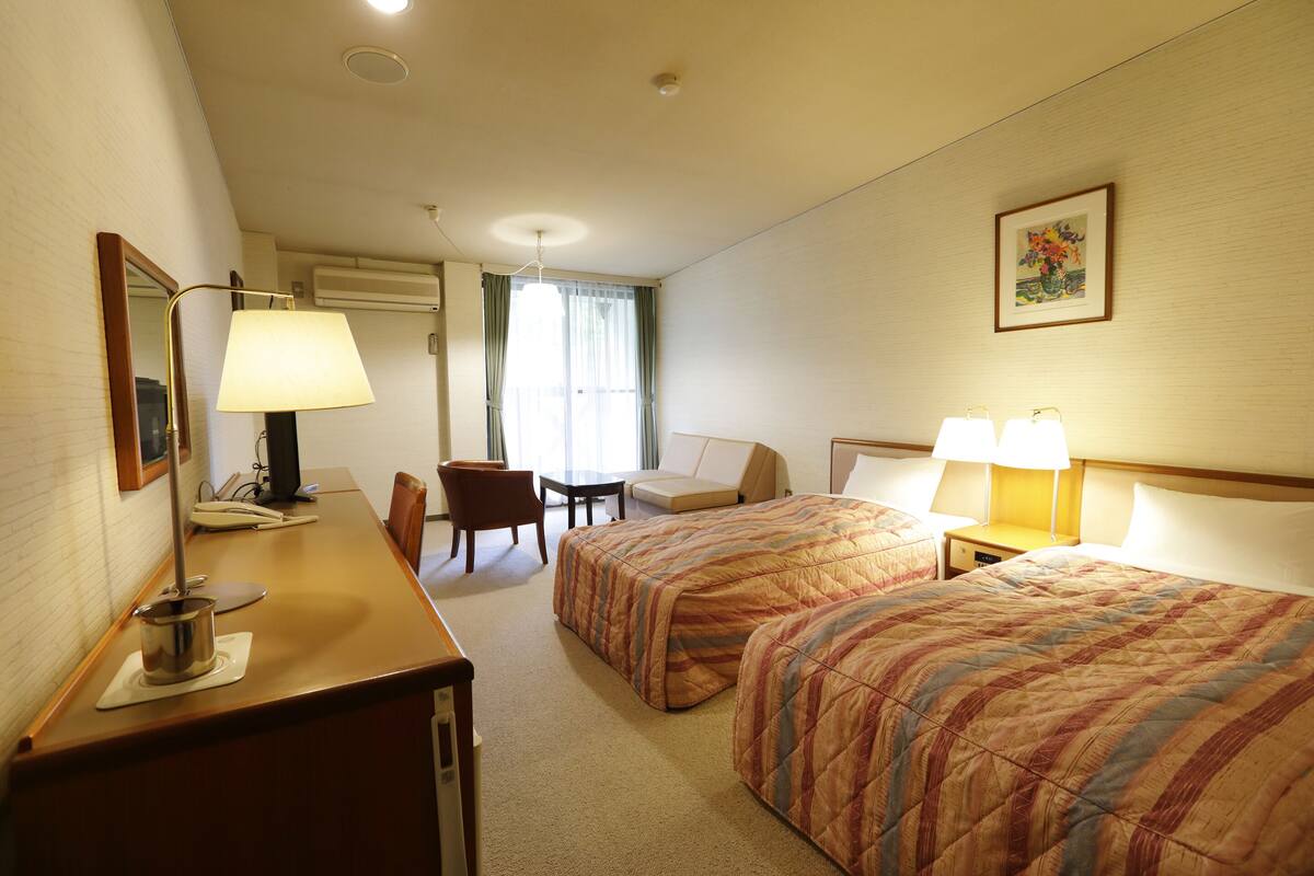 Une chambre d’hôtel avec deux lits, un bureau, une chaise, une table et une lampe.