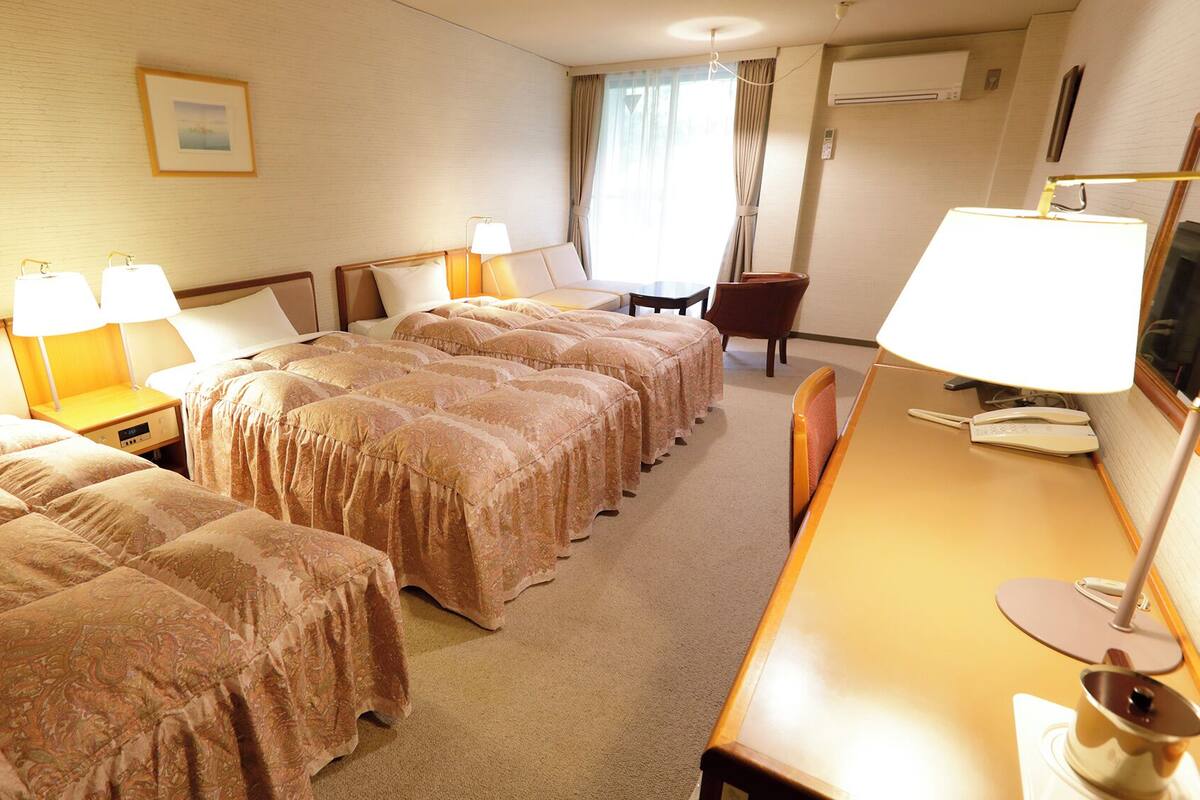 Une chambre d’hôtel avec deux lits, un bureau avec une lampe, une chaise, une télévision et une fenêtre avec des rideaux.