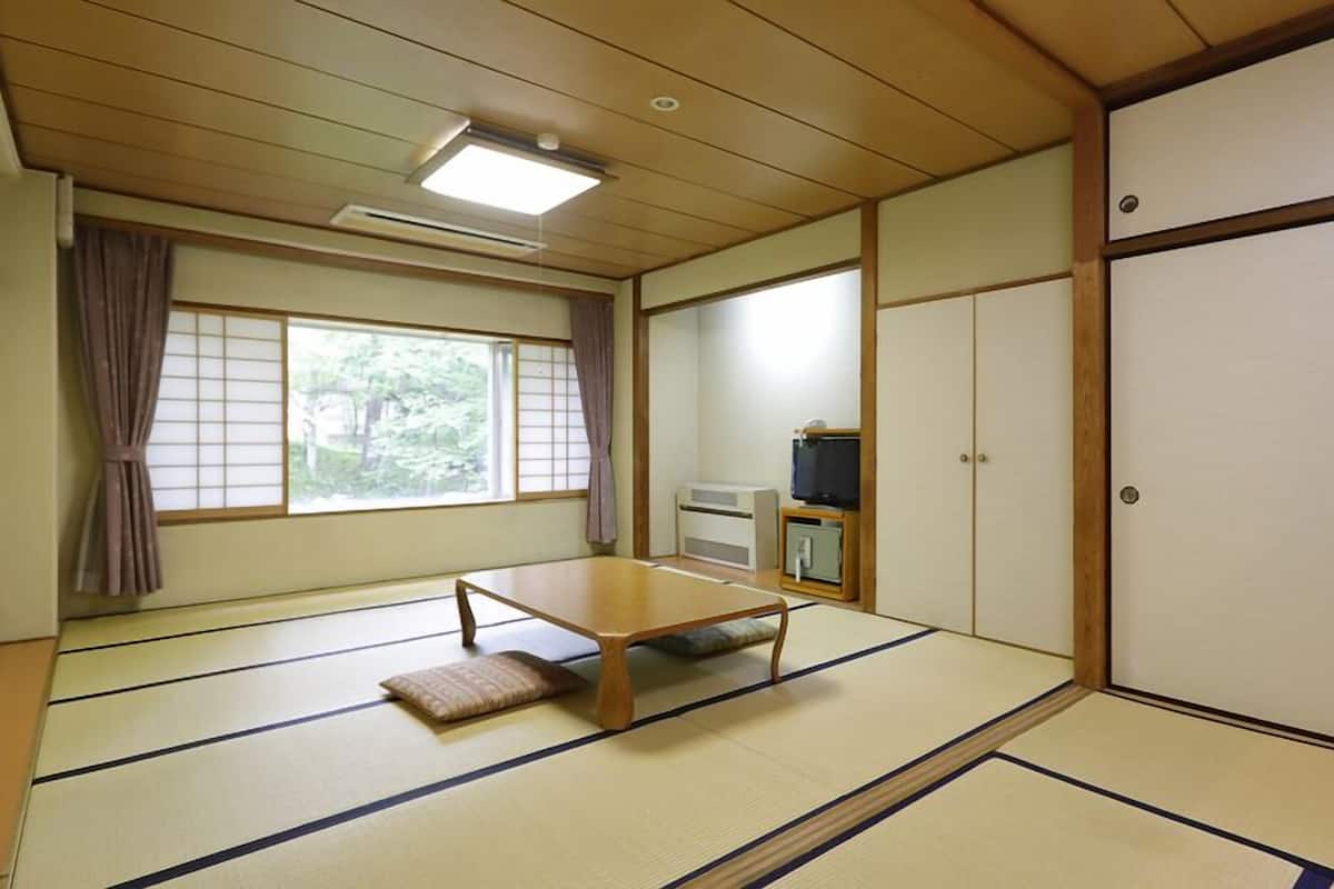 A traditional Japanese room with tatami flooring, a low table, sliding doors, and a television.