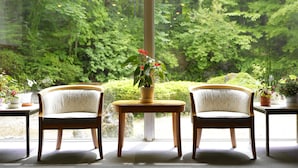 A room with two chairs facing a large window, a small table with a potted plant, and a view of a lush green forest. - Yamanakako-Asahigaoka-Onsen Hotel Seikei (Yamanakako)