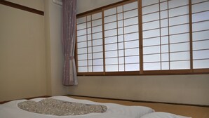 A traditional Japanese-style room with tatami flooring, a futon bed, a shoji screen, and a hanging purple curtain. - Yamanakako-Asahigaoka-Onsen Hotel Seikei (Yamanakako)