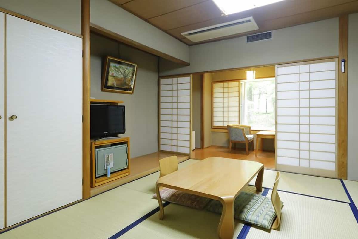 A traditional Japanese room with tatami flooring, a low table, a television on a cabinet, and sliding doors.
