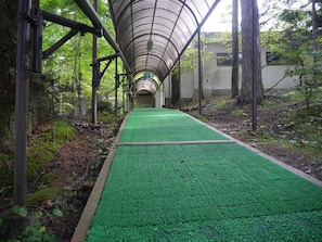 A covered walkway with a green surface, surrounded by trees and vegetation. - Yamanakako-Asahigaoka-Onsen Hotel Seikei (Yamanakako)