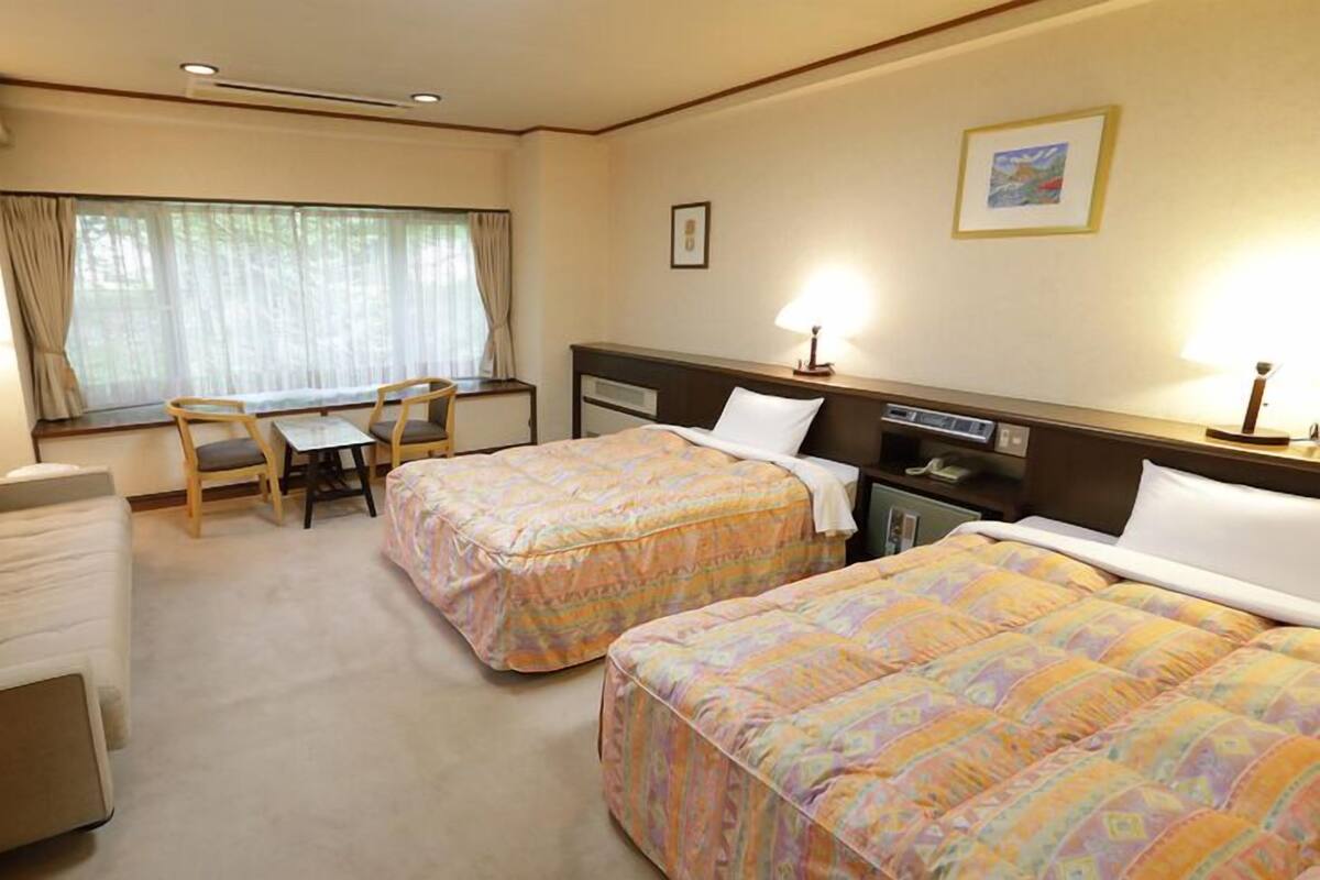 Une chambre d’hôtel avec deux lits, un bureau, une chaise et un canapé.