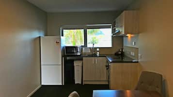 A compact kitchen with a refrigerator, microwave, sink, and a window overlooking greenery.