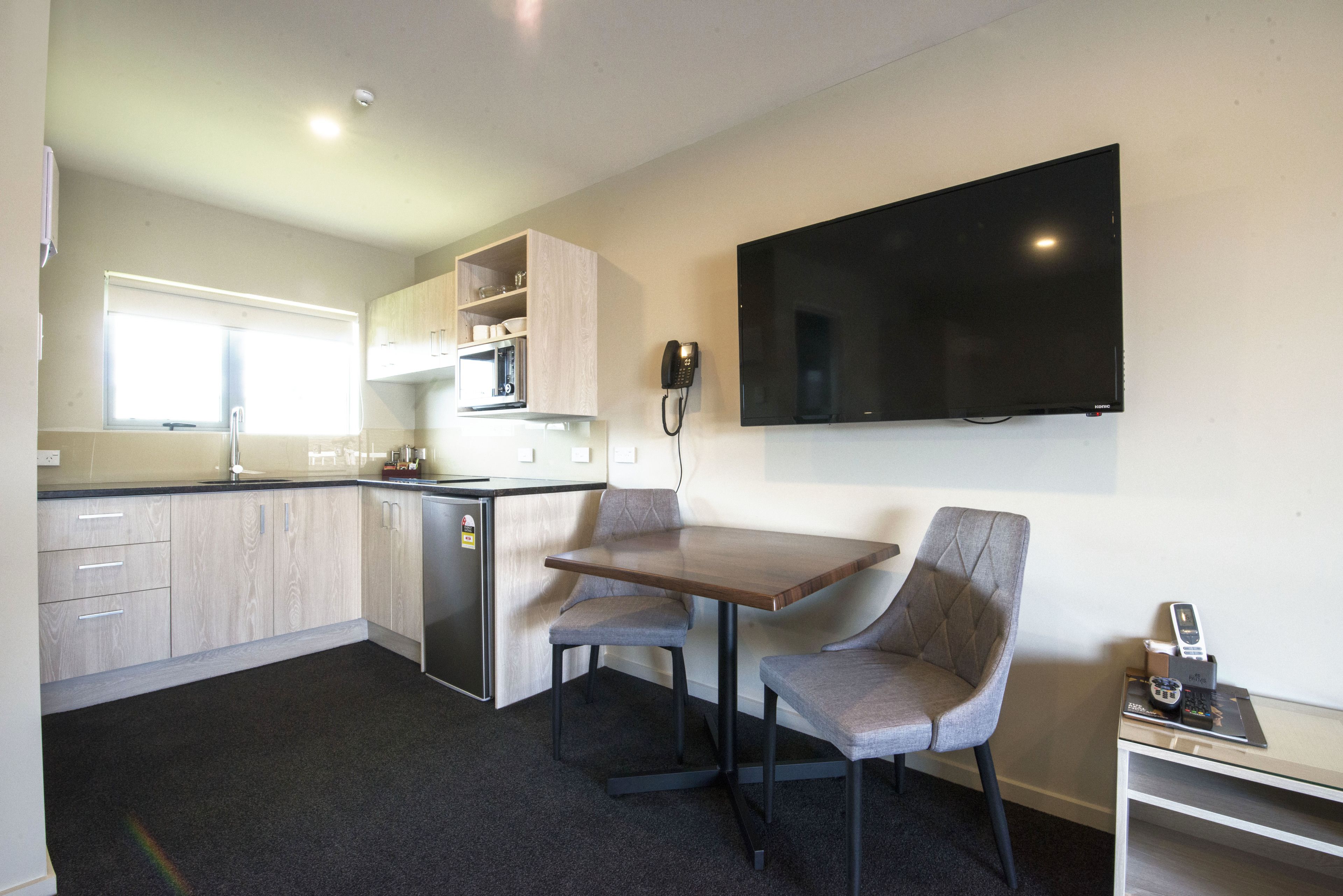 A compact kitchen with a dining area, a microwave, and a flat-screen TV mounted on the wall.