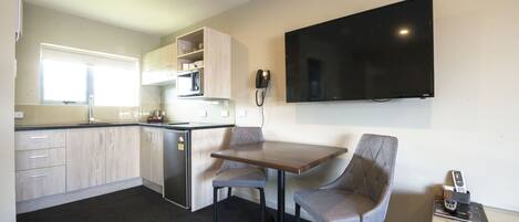 A compact kitchen with a dining area, a microwave, and a flat-screen TV mounted on the wall.