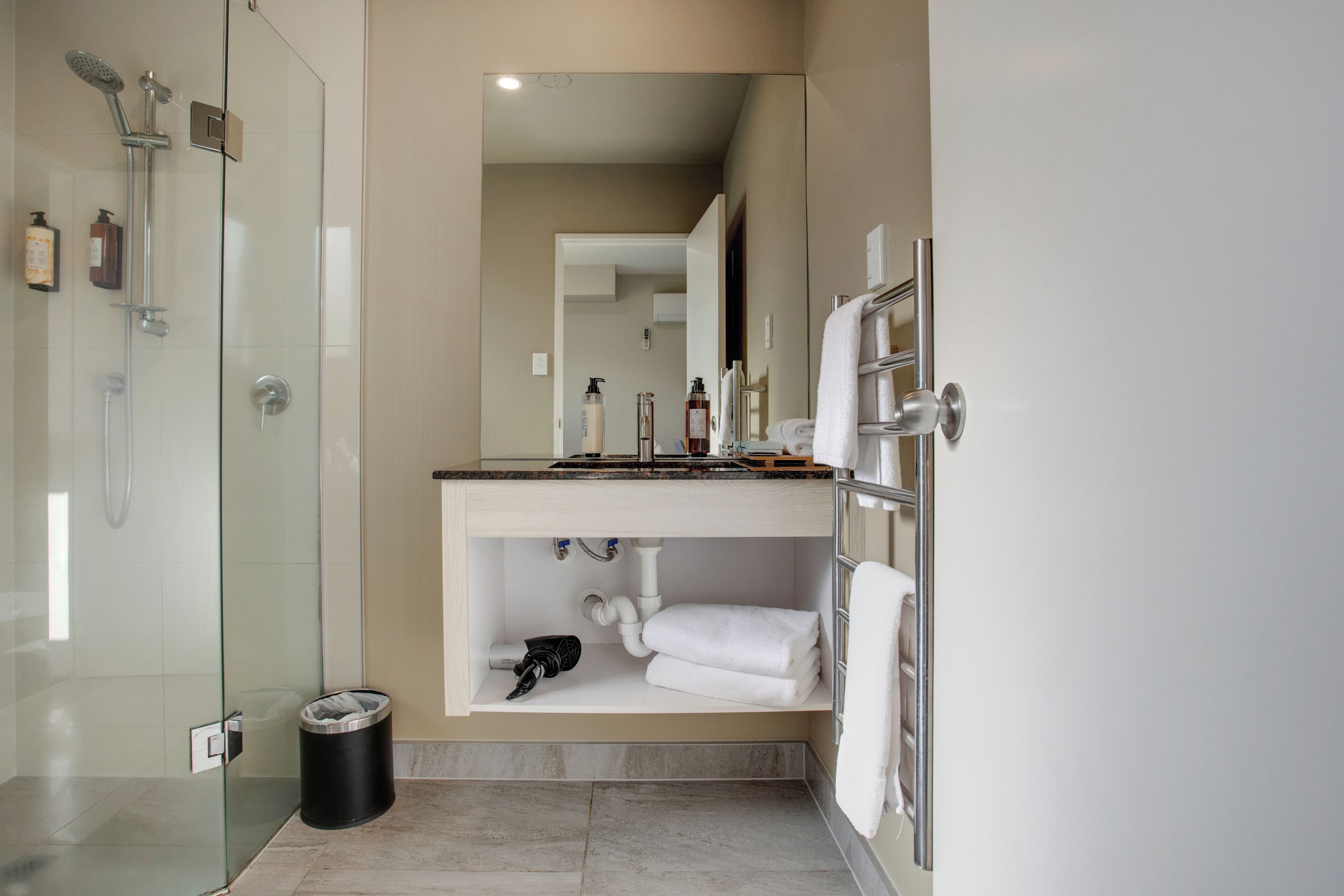 Uma casa de banho moderna com chuveiro em cabine de vidro, toucador com espelho e porta-toalhas.