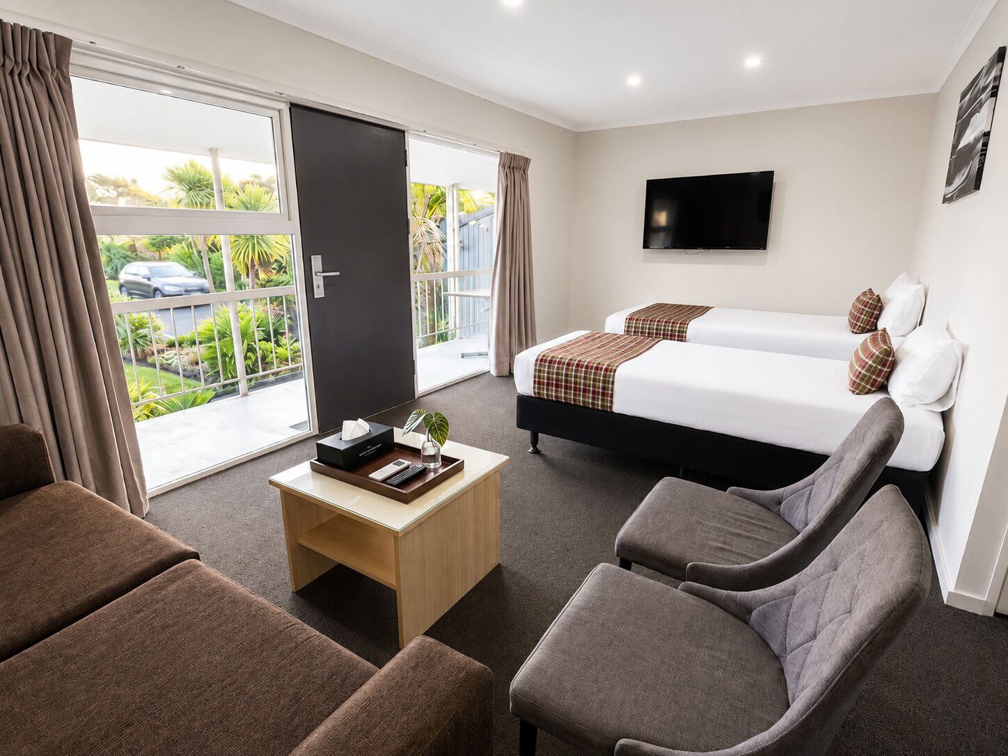 A hotel room with a bed, a desk, two armchairs, a TV, and a view of the outdoors.