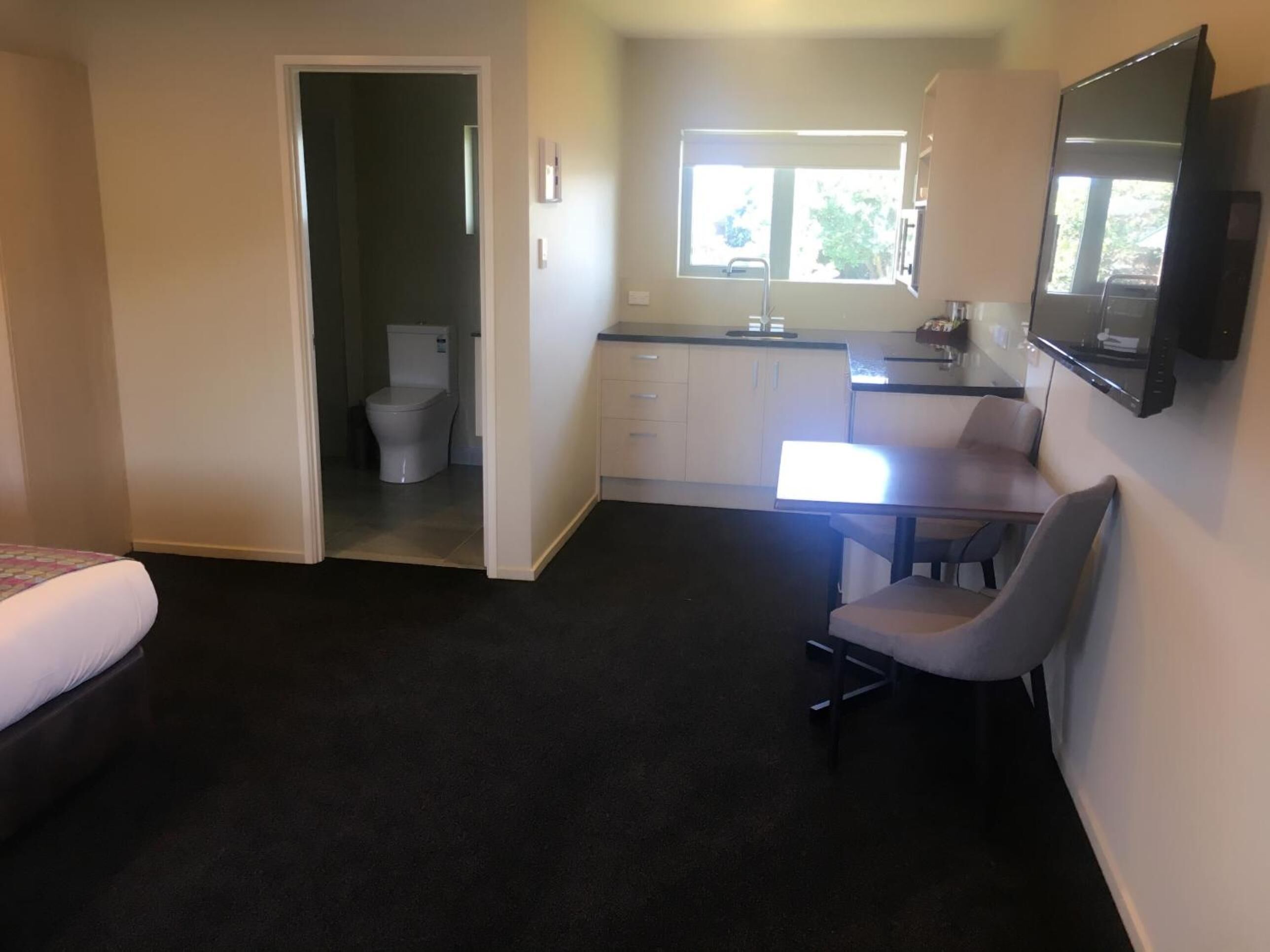 Habitación de hotel compacta con cama, kitchenette pequeña, zona de comedor y baño.