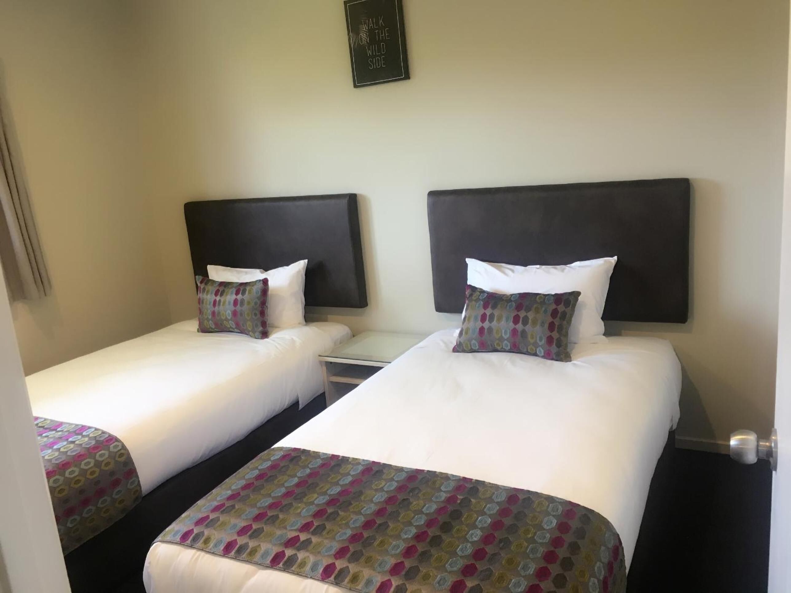 Een hotelkamer met twee eenpersoonsbedden, elk met een hoofdeinde, nachtkastje en kussen.