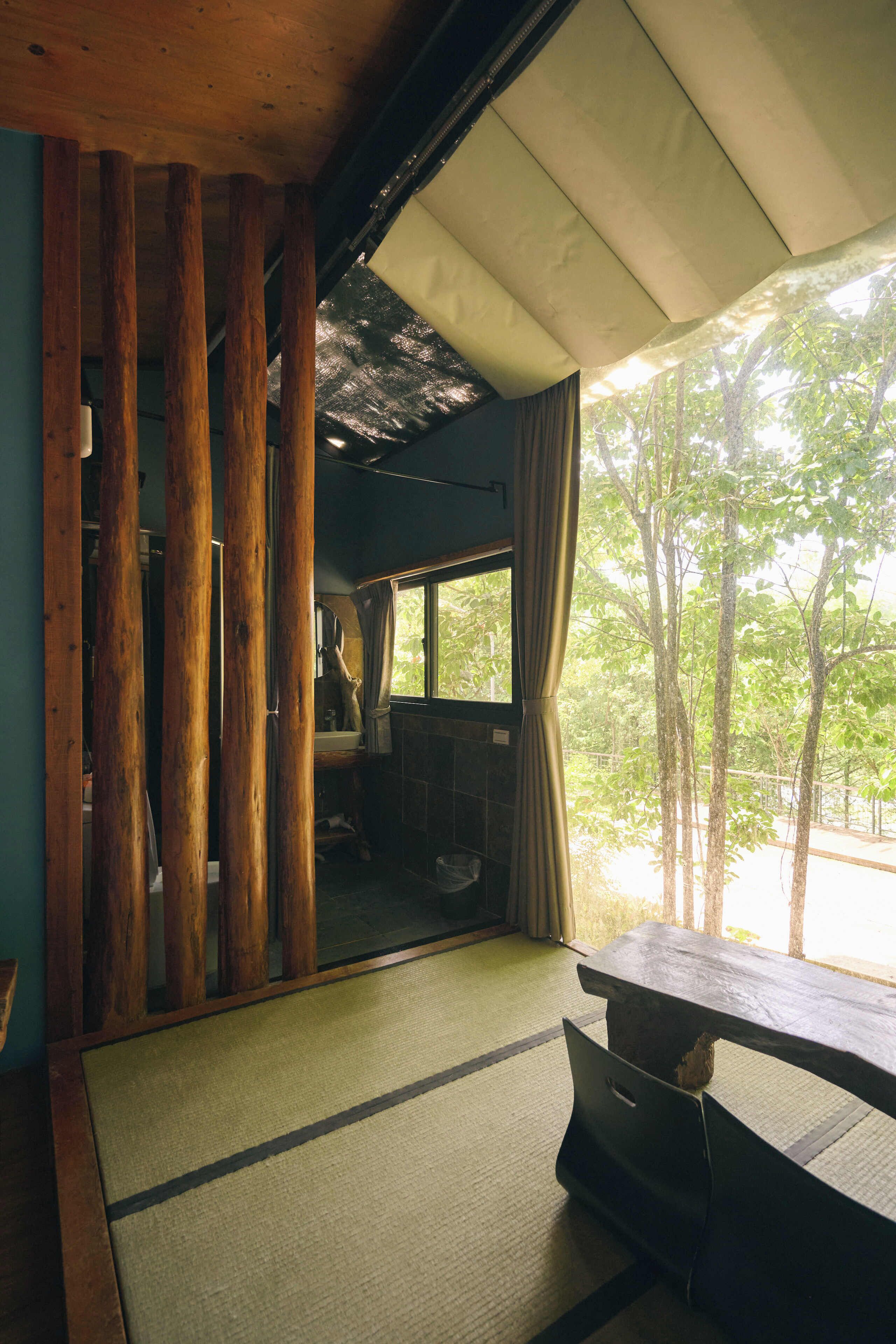 Una habitación japonesa tradicional con suelo de tatami, una mesa de madera baja y vistas a árboles a través de una ventana.