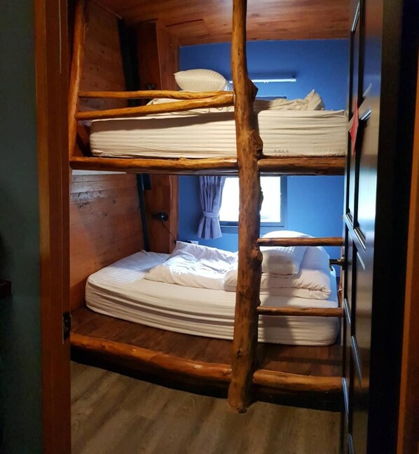 Quarto com beliche de madeira, janela com cortinas e porta visível.