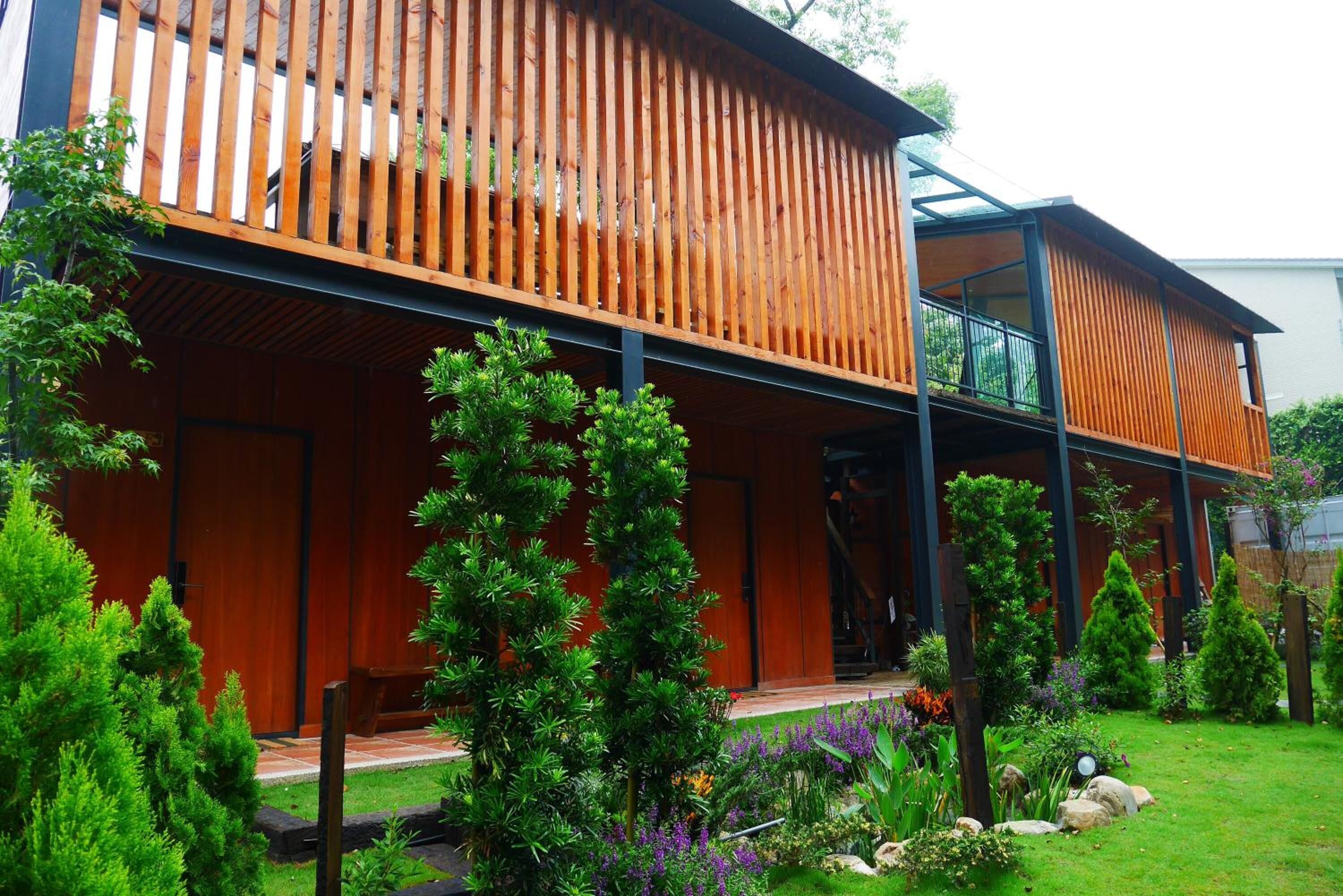 A modern house with a wooden balcony, a wooden deck, and a well-maintained garden with various plants and shrubs.