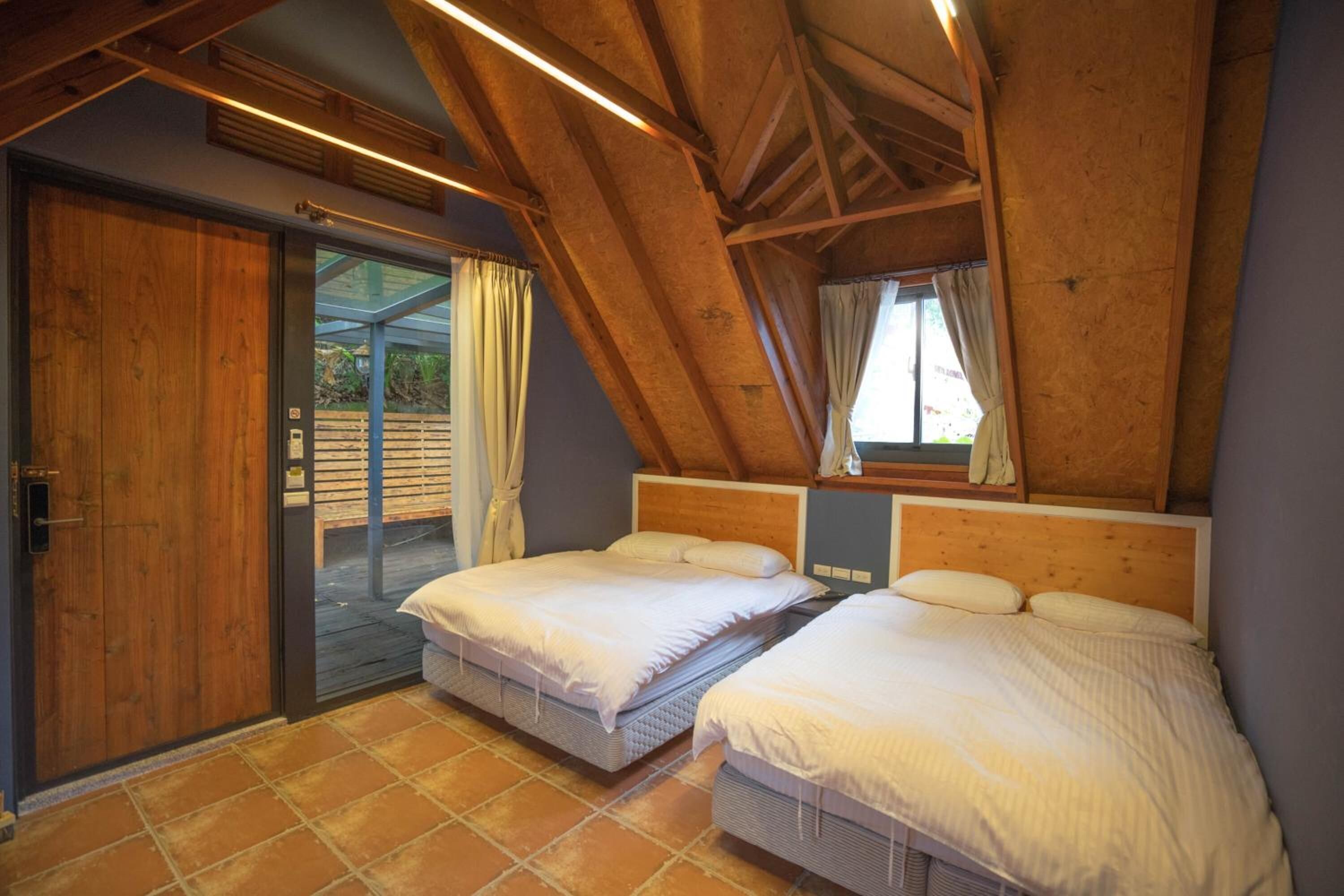 Ein Schlafzimmer mit zwei Betten, einer Holzbalkendecke und einer Schiebeglastür, die zu einem Außenbereich führt.