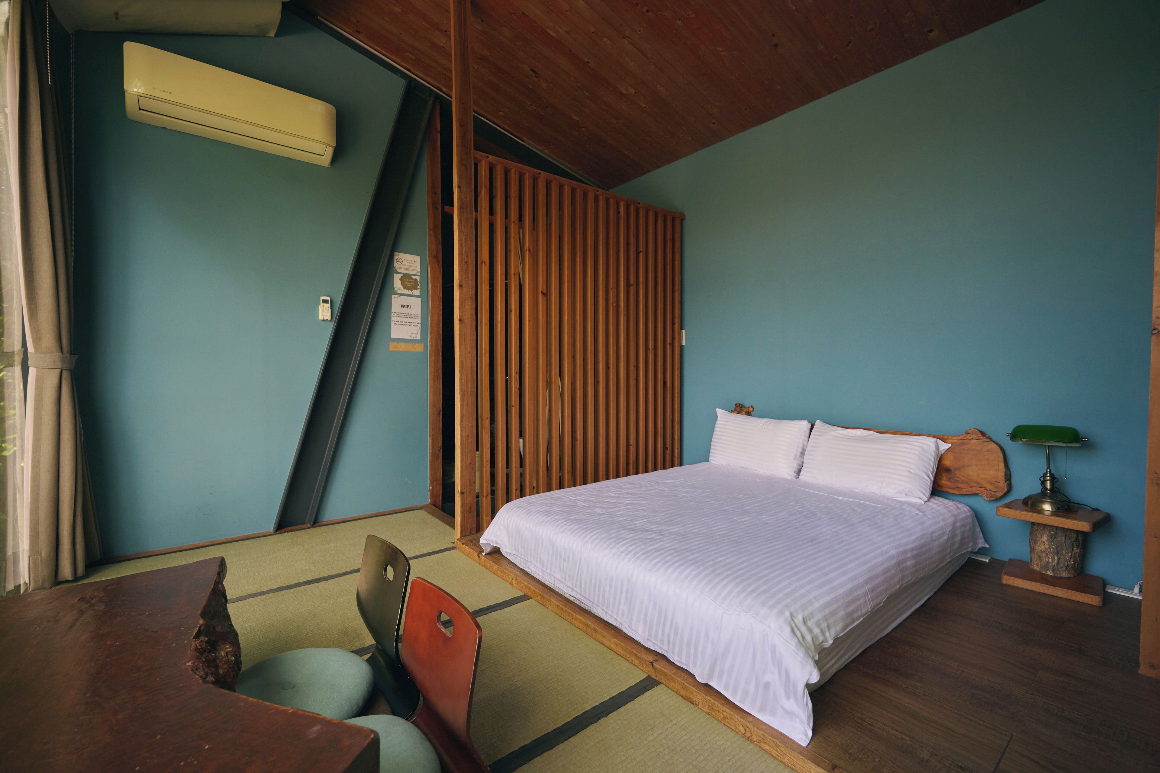 A bedroom with a bed, a wooden headboard, a nightstand with a lamp, a chair, and a desk.