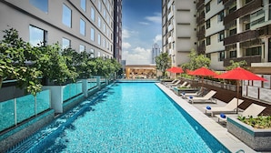 Una piscina con sillas de descanso y sombrillas, rodeada de edificios altos.