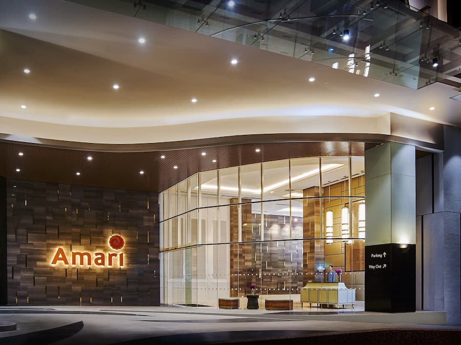 Una entrada de hotel moderna con fachada de vidrio, un llamativo letrero 'Amari' y un mostrador de recepción.