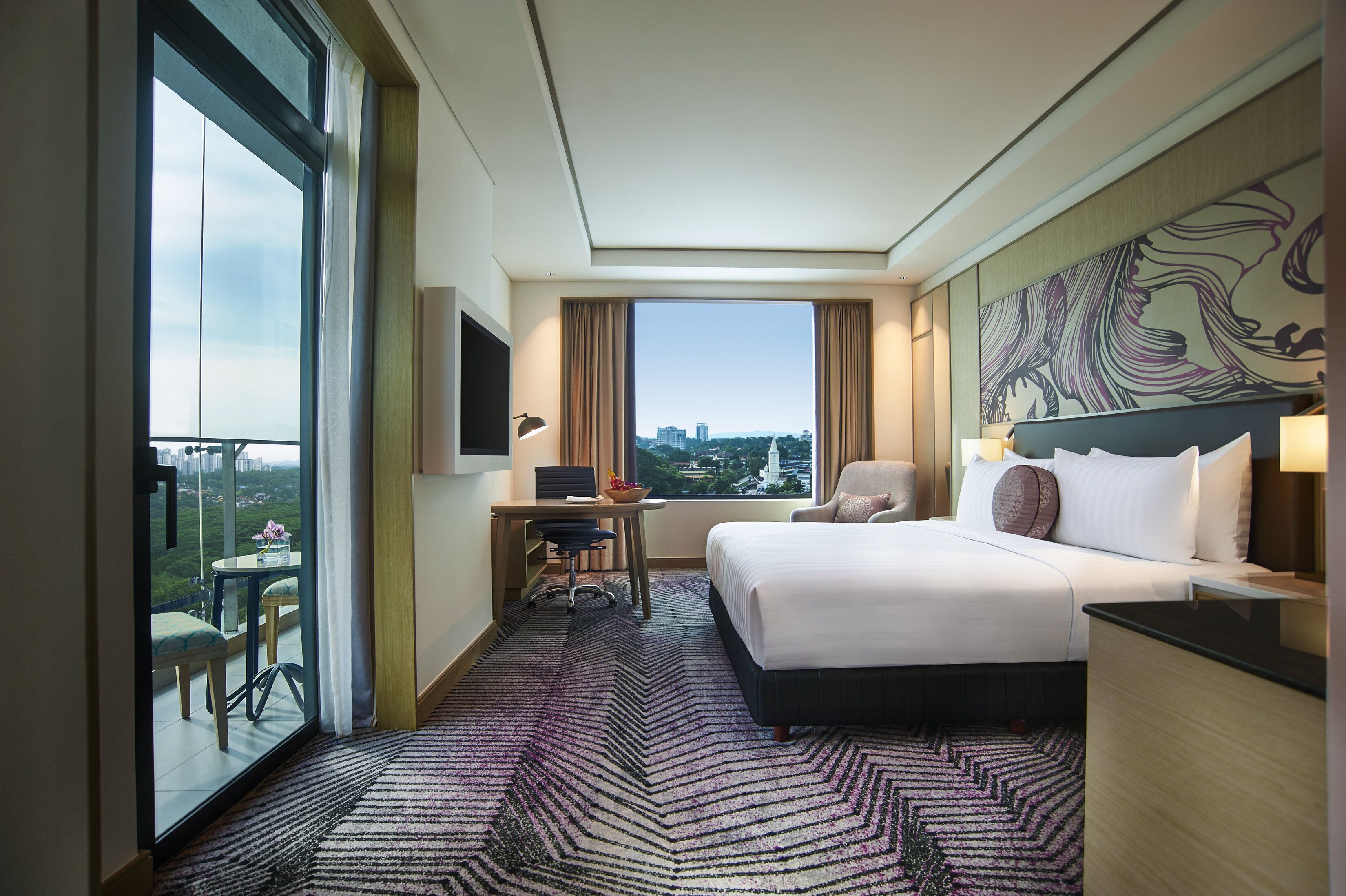 A hotel room with a bed, desk, chair, and a large window with a city view.