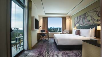 A hotel room with a bed, desk, chair, and a large window with a city view.