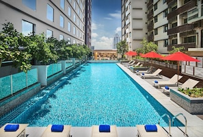 A swimming pool with lounge chairs and umbrellas, surrounded by high-rise buildings.