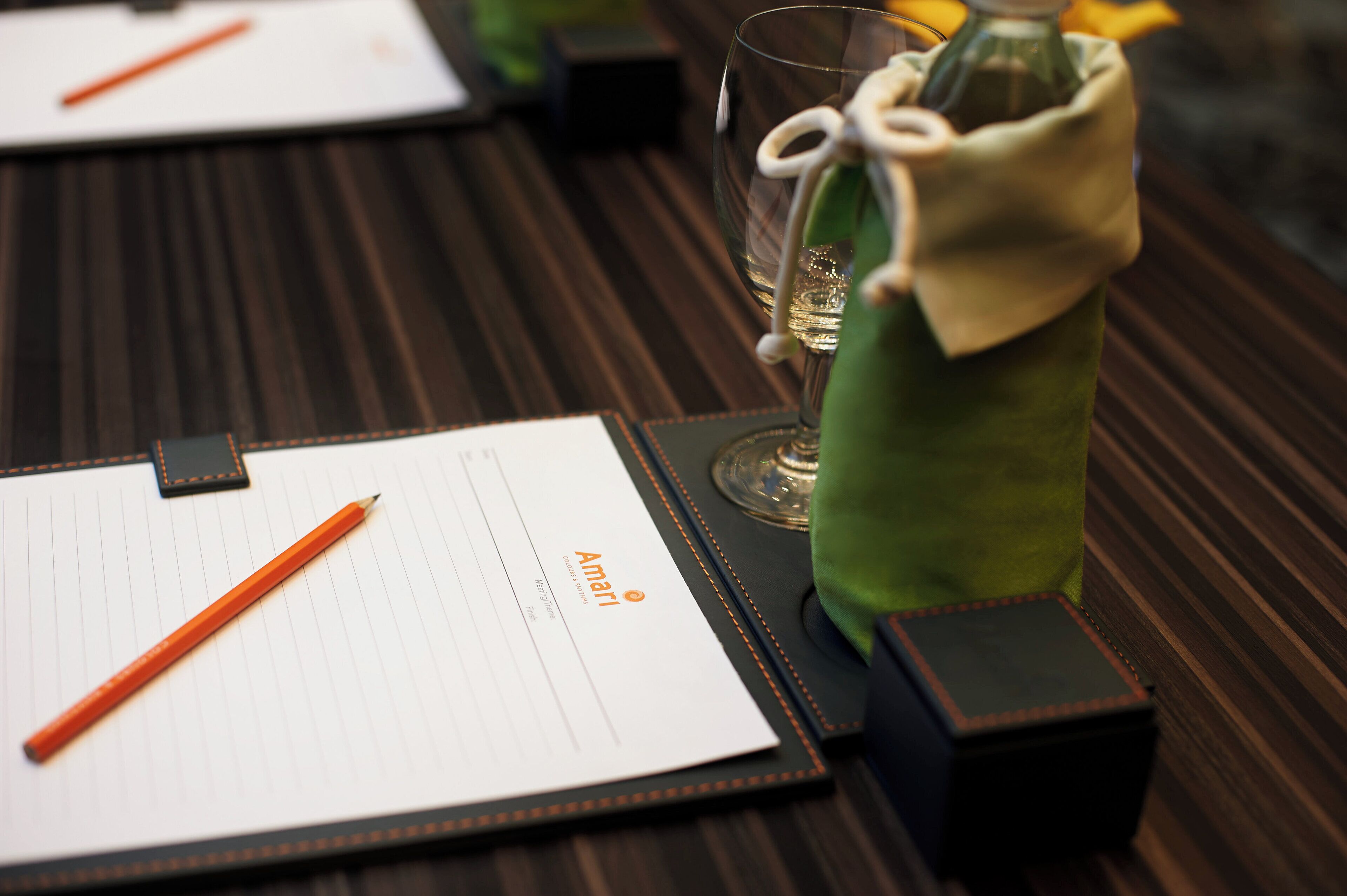 A neatly arranged table with a notepad, pencil, glass, and a bottle wrapped in a cloth.