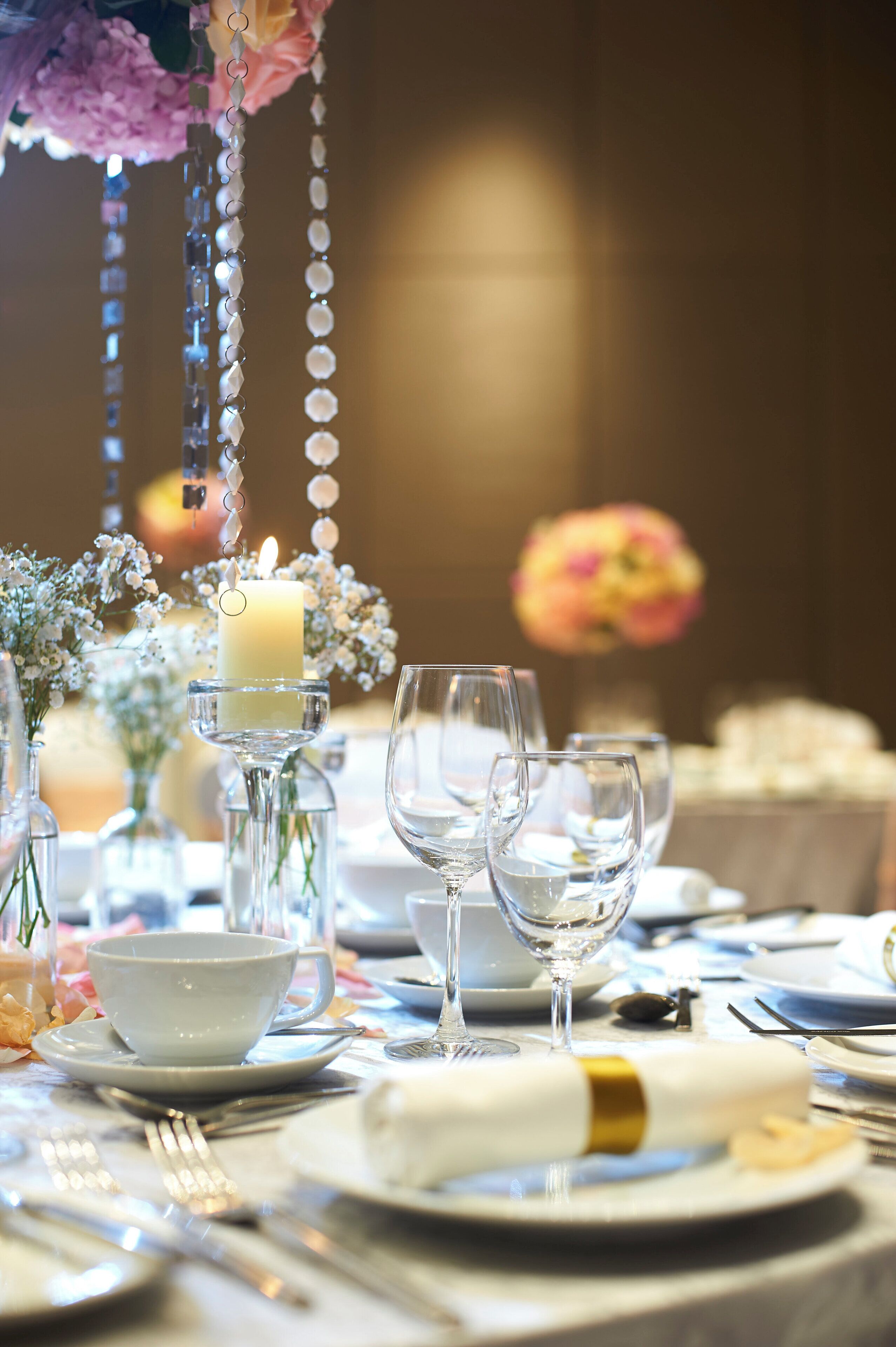 Una mesa dispuesta para una cena formal, con copas de cristal transparente, un centro de mesa con velas y arreglos florales.
