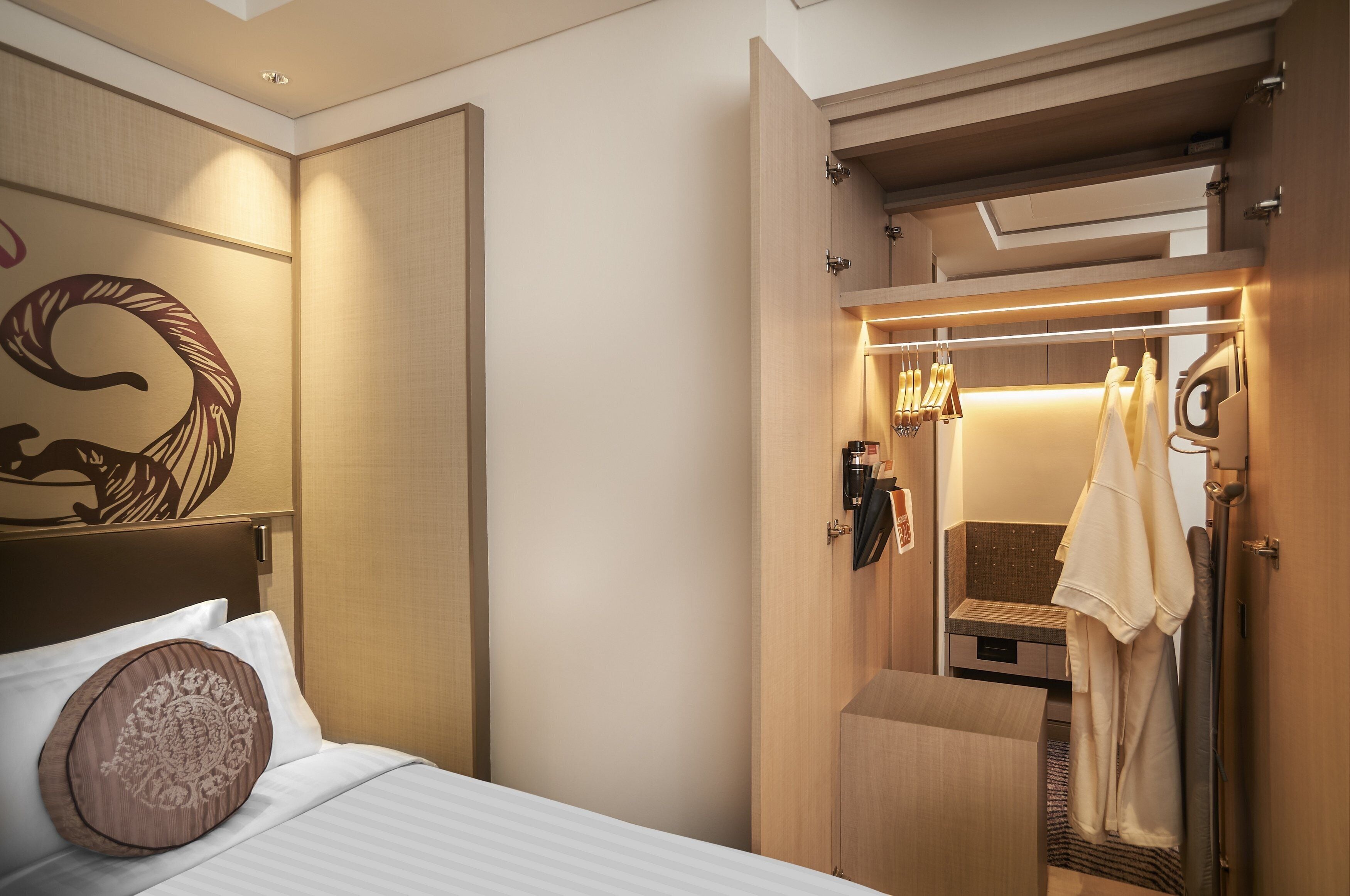 Una habitación de hotel con una cama, cabecera de madera, un espejo y una bata colgada en un perchero.