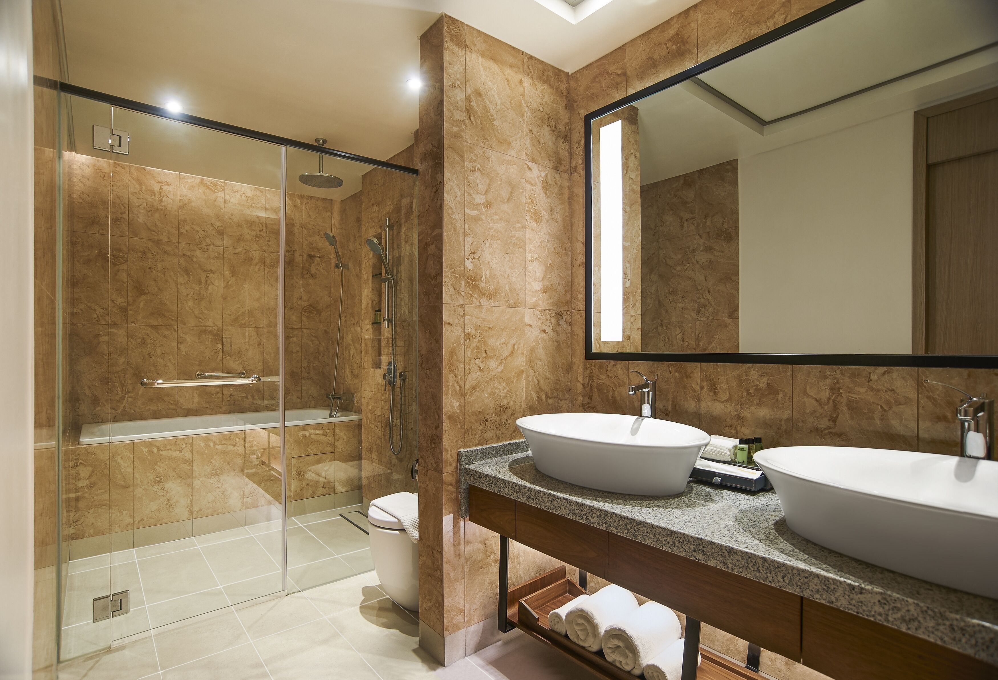 Un baño moderno con ducha de vidrio, dos lavamanos y un espejo grande.