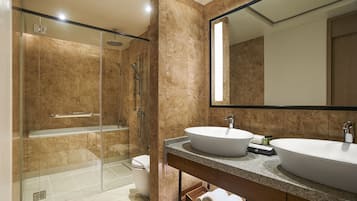 Un baño moderno con ducha de vidrio, dos lavamanos y un espejo grande.