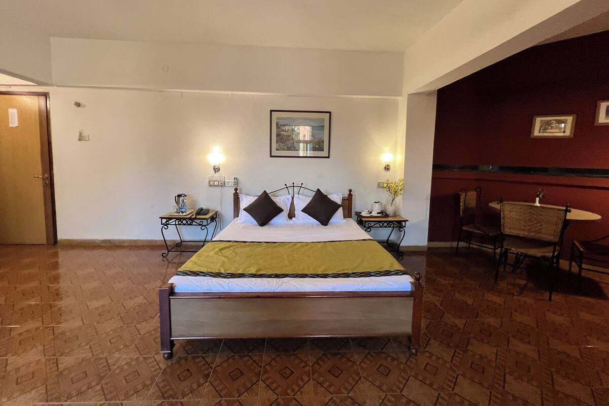 Une chambre d’hôtel comprenant un lit, deux tables de chevet, une chaise, un ventilateur de plafond et un tableau accroché au mur.