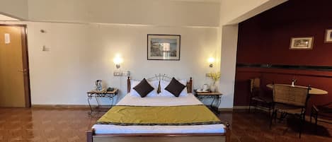 Habitación de hotel con cama, dos mesitas de noche, una silla, ventilador de techo y un cuadro colgado en la pared.