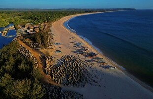 Vista aérea de una zona costera con playa, barcos y un pequeño poblado.