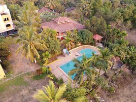 Zona residencial con piscina rodeada de palmeras y una casa con techo de tejas.