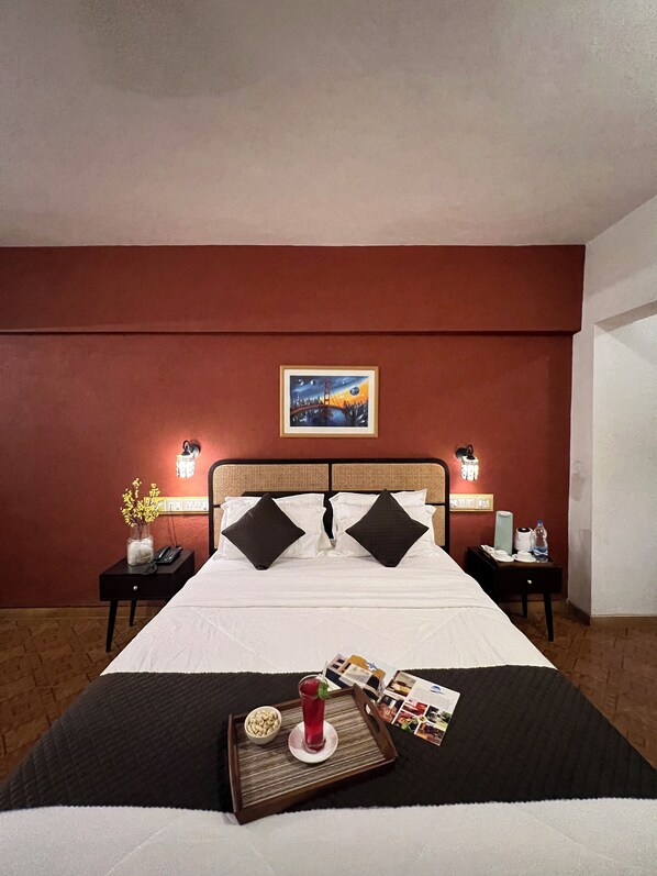 A hotel room with a large bed, two nightstands, a painting on the wall, and a tray with a drink and snacks on the bed.