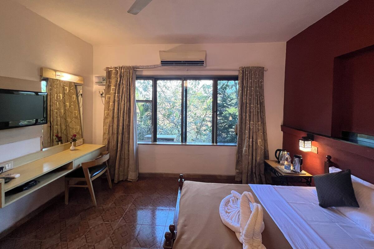 Une chambre d’hôtel équipée d’un lit, d’un bureau, d’une télévision, d’une fenêtre avec des rideaux et d’un ventilateur de plafond.