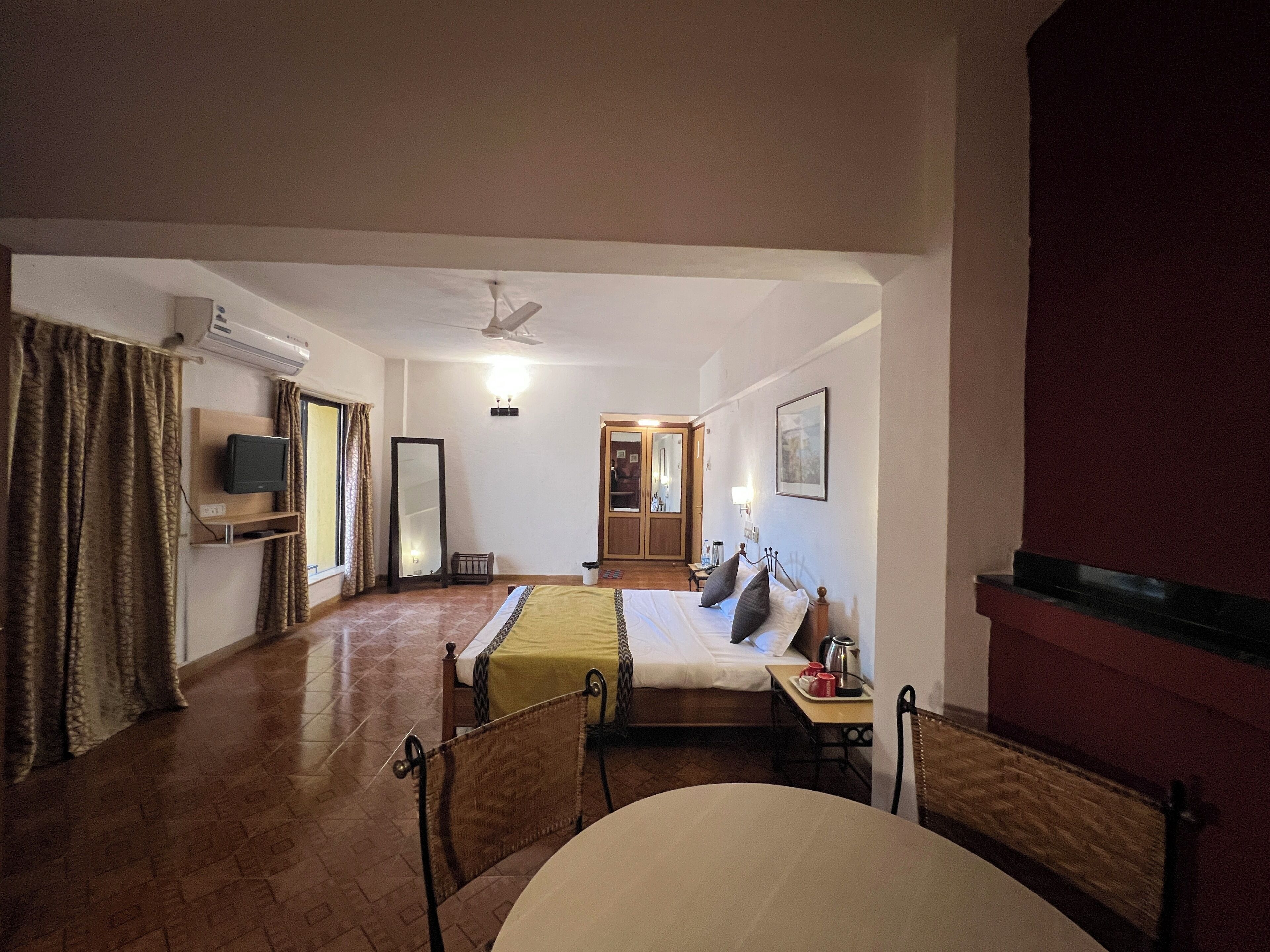 Una habitación de hotel con cama, una mesita con tazas, una silla, un televisor y un espejo.