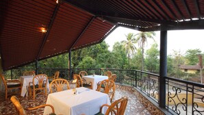Une terrasse extérieure avec des tables et des chaises, entourée d’une rambarde en métal et de palmiers.