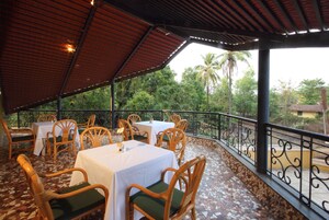 Un patio al aire libre con mesas y sillas, rodeado por una barandilla metálica y palmeras.
