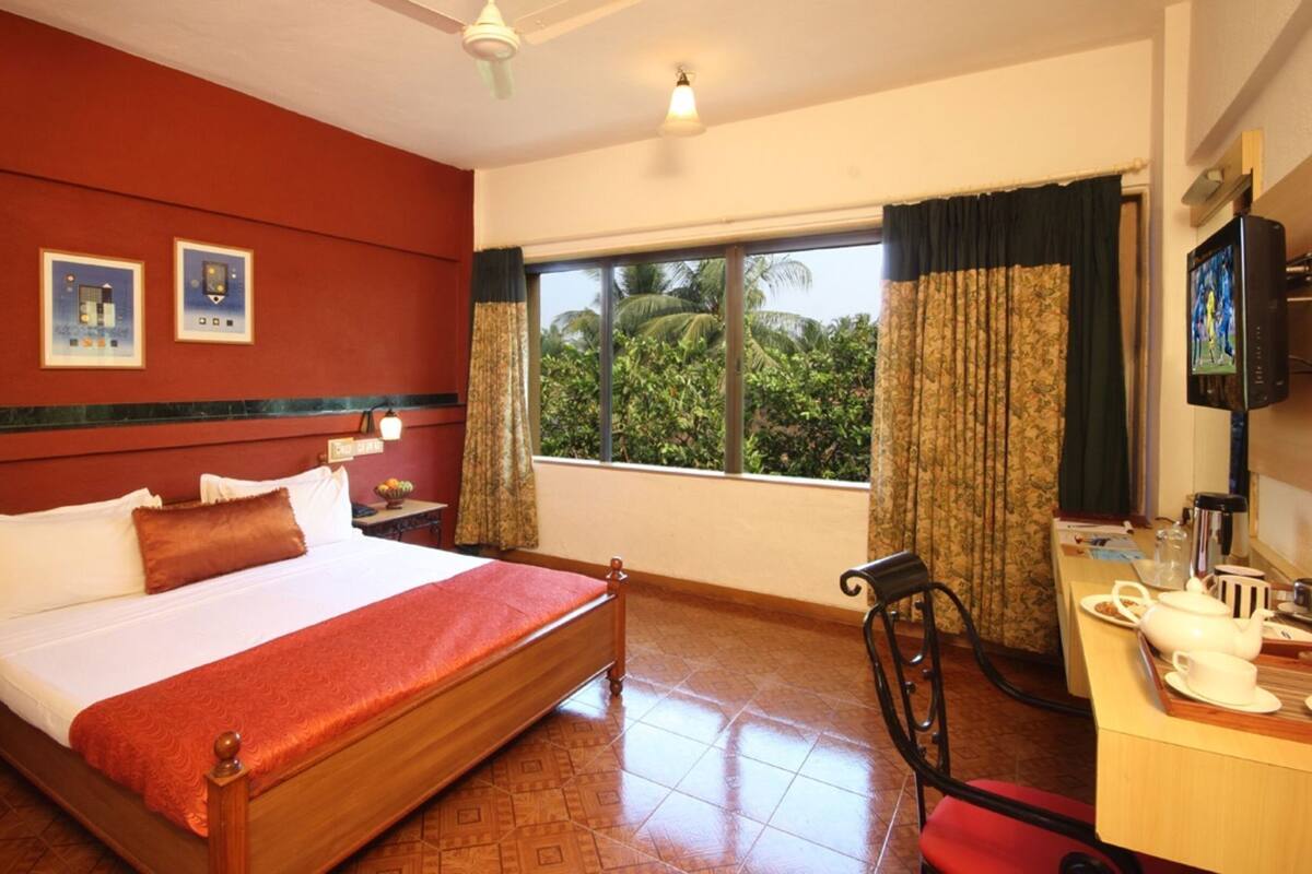 Une chambre d’hôtel comprenant un lit, un bureau avec une chaise, une télévision et une fenêtre avec des rideaux.