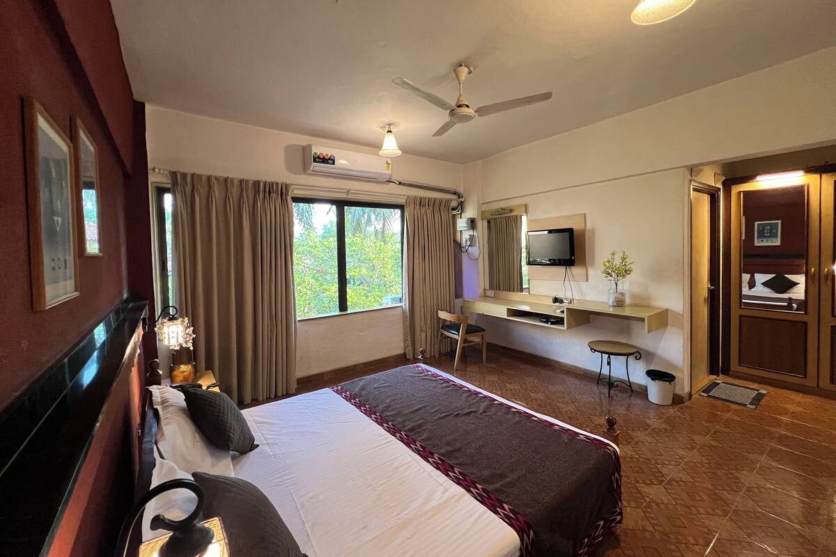 Une chambre d’hôtel équipée d’un lit, d’un bureau, d’une télévision et d’un ventilateur de plafond.