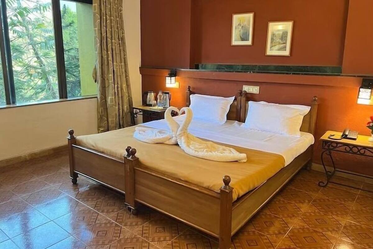 Une chambre d’hôtel avec un lit, une table de chevet, un téléphone et une fenêtre avec des rideaux.